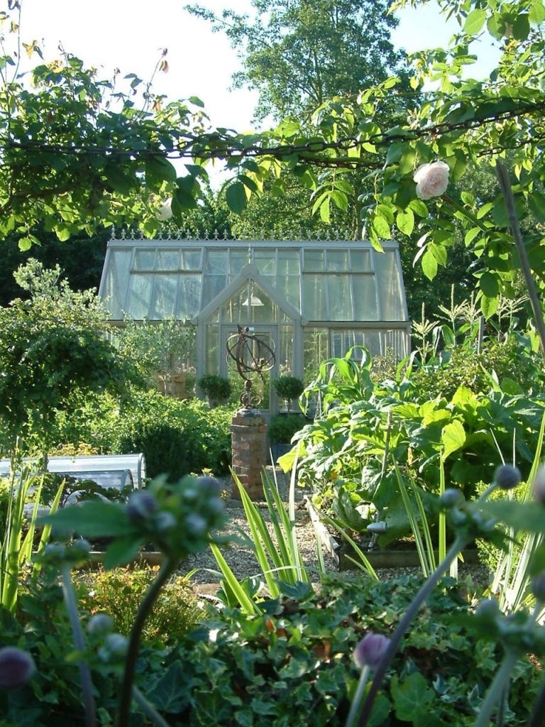 Greenhouse hidden behind summer roses and garden ornament