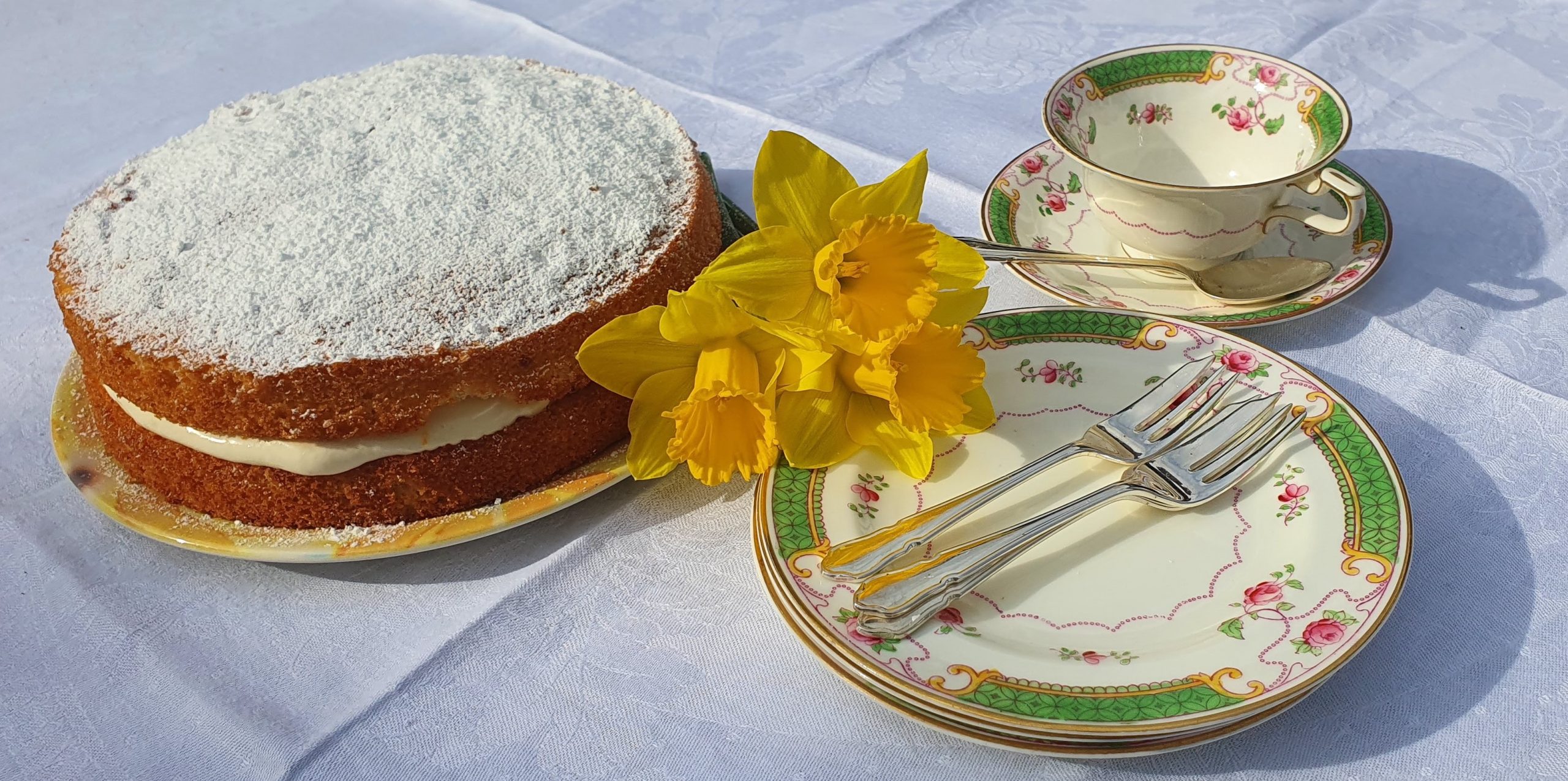 Lemon cake decorated with a daffodil, with plates and cups beside it